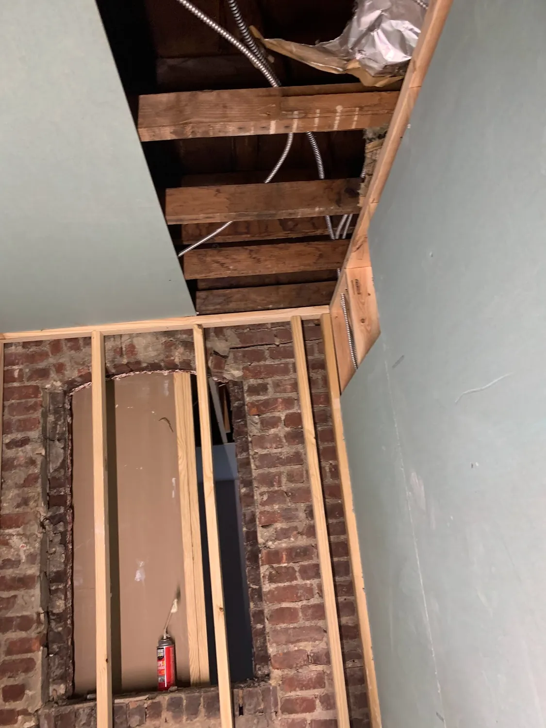 Bare wood framing, exposed brick, and open ceiling joists before the bathroom build-out