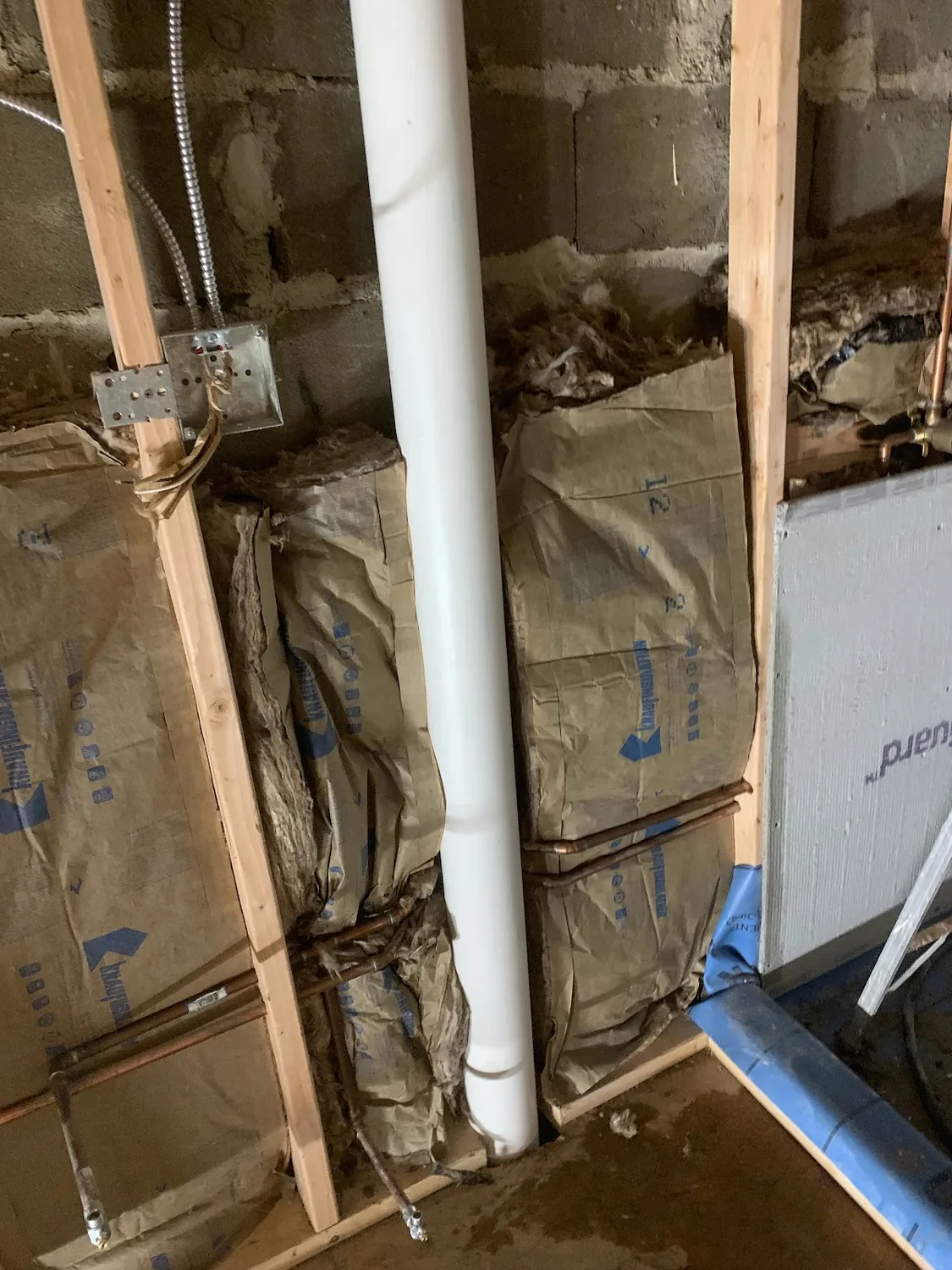 Bathroom rough-in with water supply, PVC drain stack, and electrical against bare masonry before walls and tile