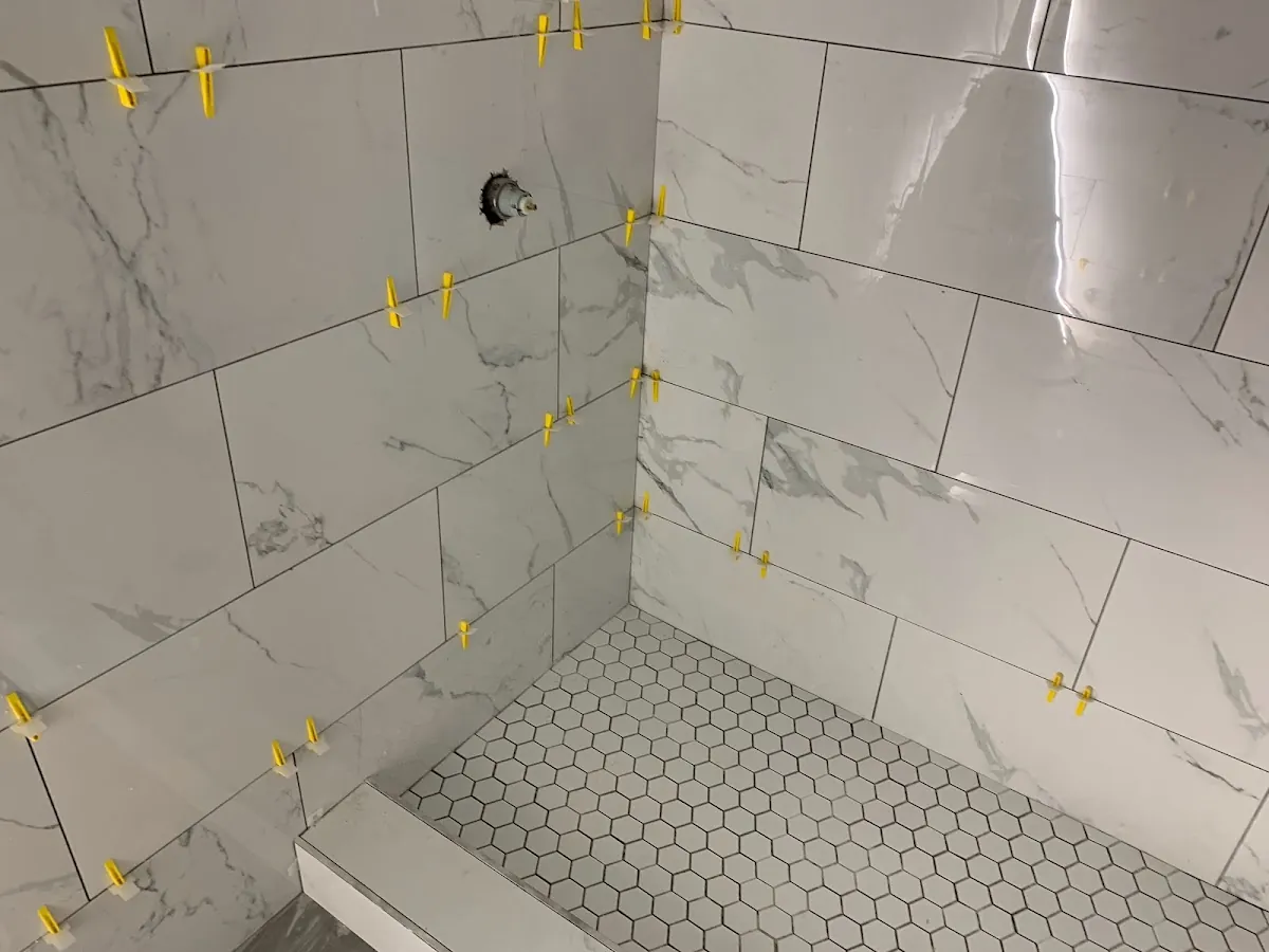 Marble-look shower walls, built-in bench, and white hexagon mosaic shower floor taking shape