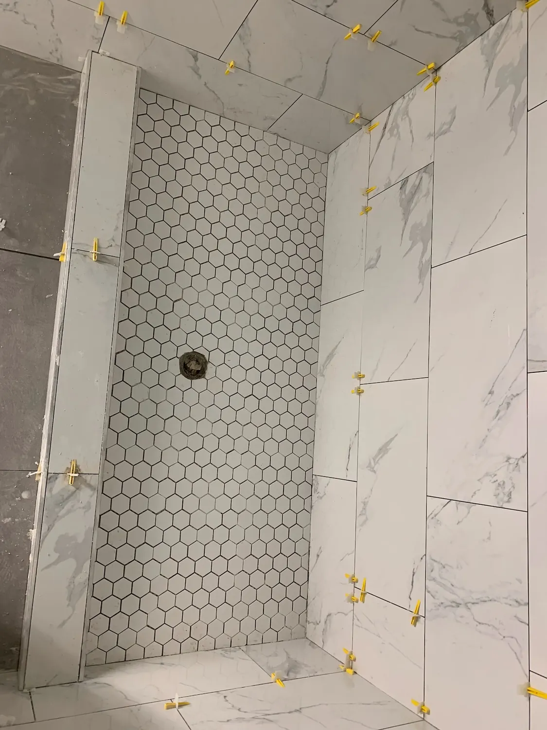Marble-look tiled shower with recessed niche, bench, and white hexagon mosaic floor in Queens