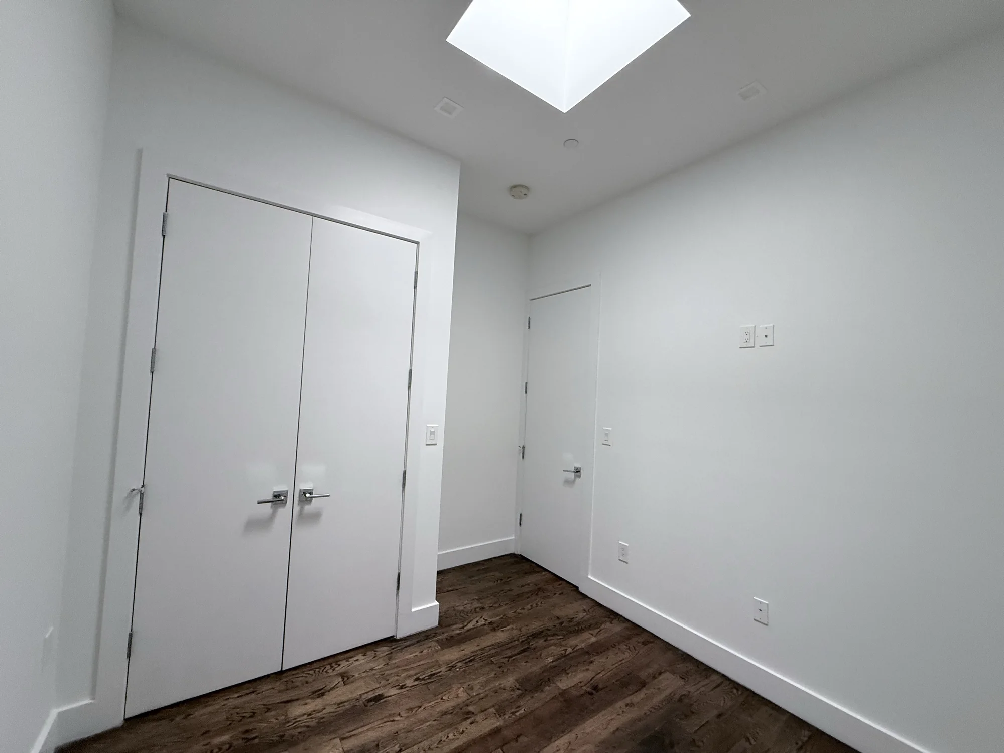 Bright white room with skylight and wood floor before painting, Brooklyn