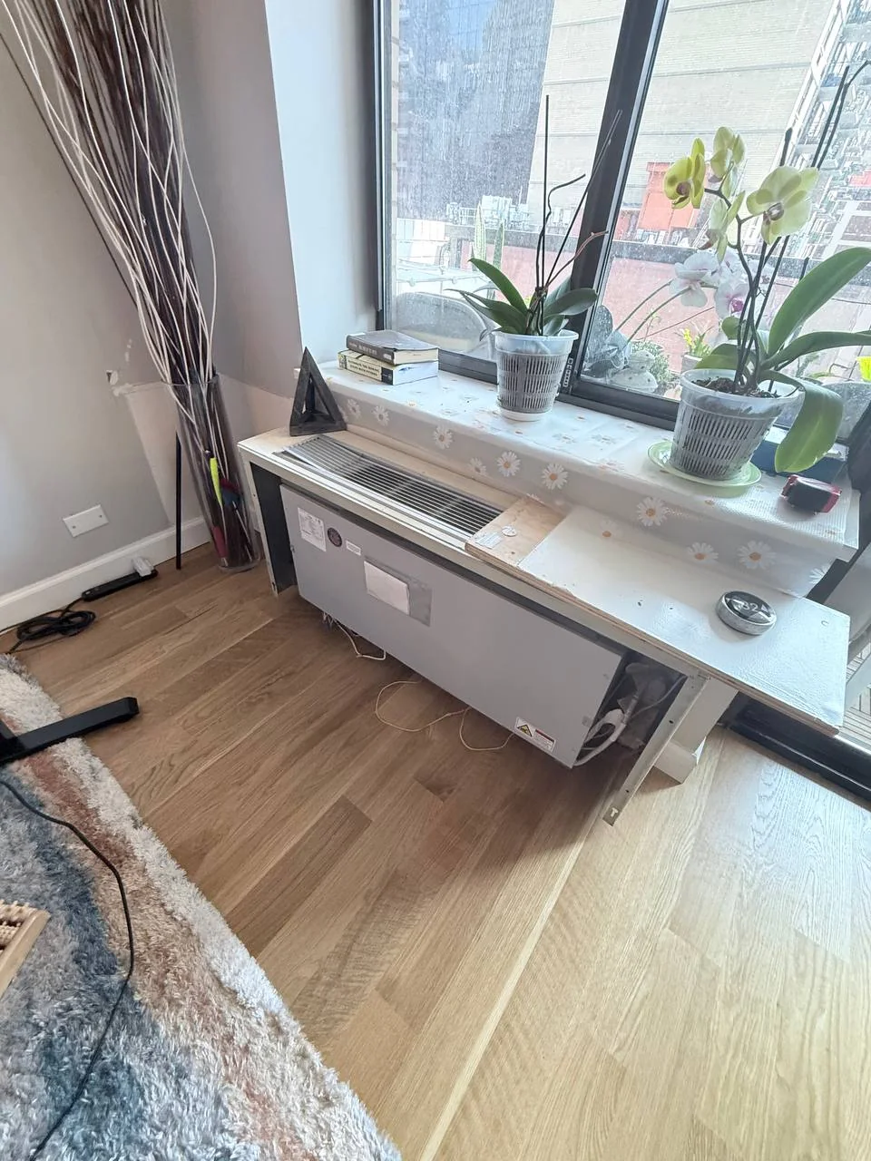 Exposed under-window AC unit with loose wires and a plywood sill after a flood, NYC high-rise apartment