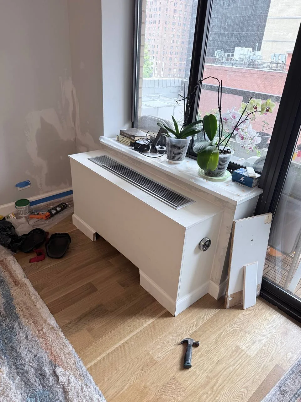 The same window with a custom white AC cover box installed on day one, patched wall beside it, NYC high-rise apartment