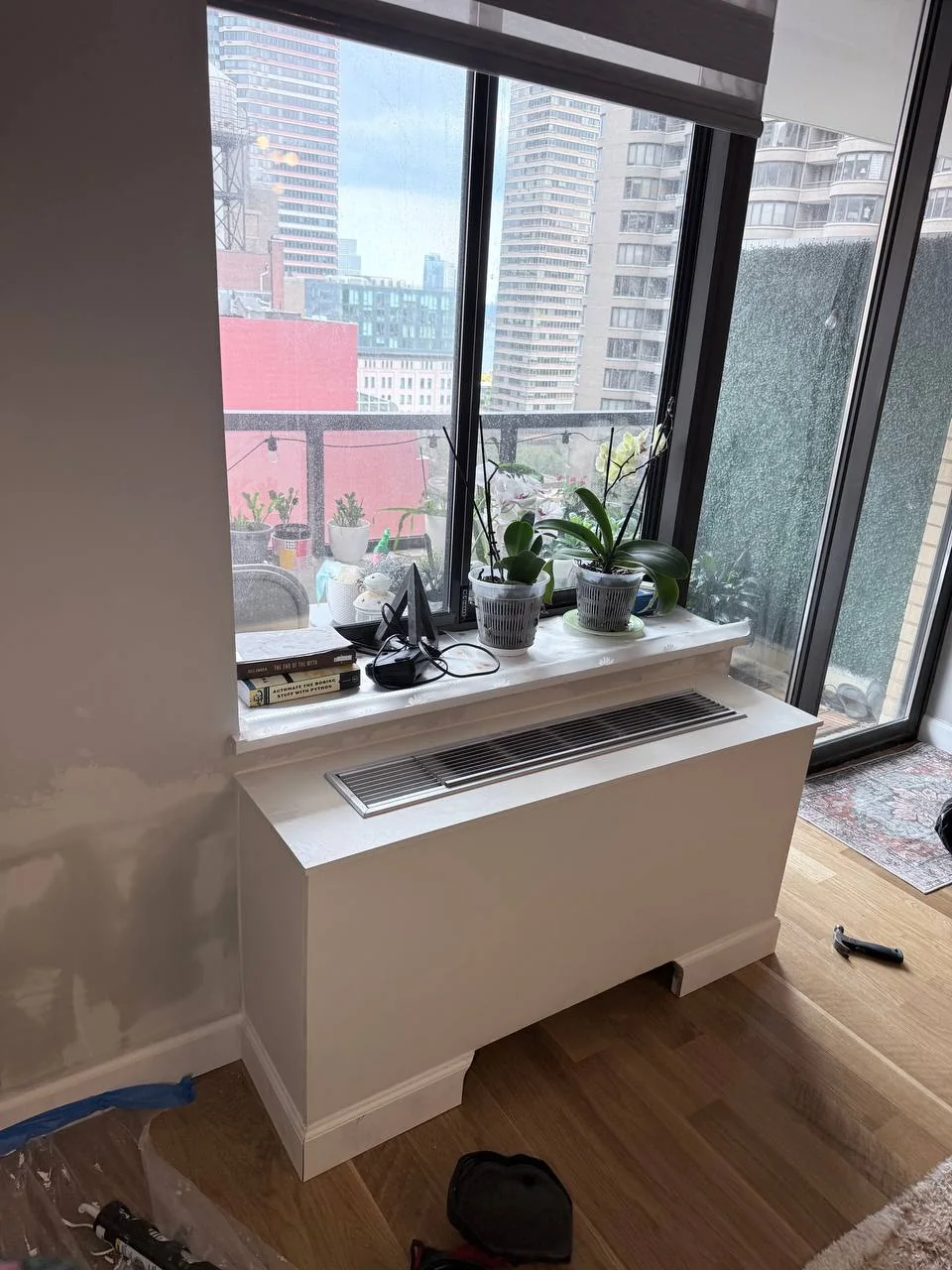 Custom AC cover box with a vented top grille under a window with a city skyline view, NYC high-rise apartment