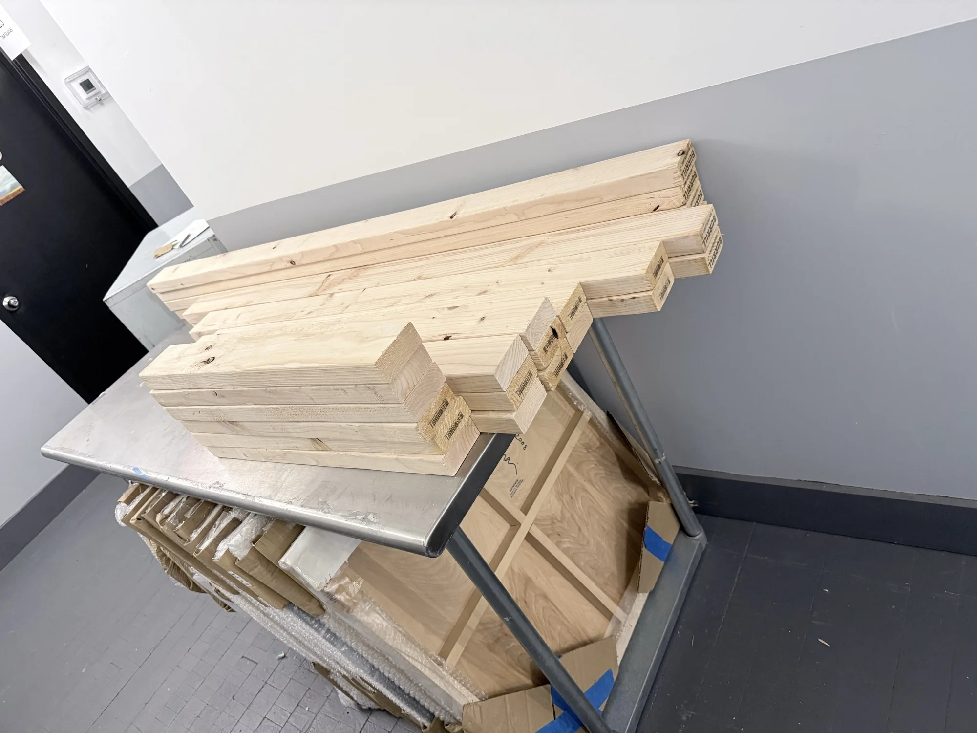 Stack of pre-cut 2x4 lumber and plywood on a cart ready to be carried into the studio