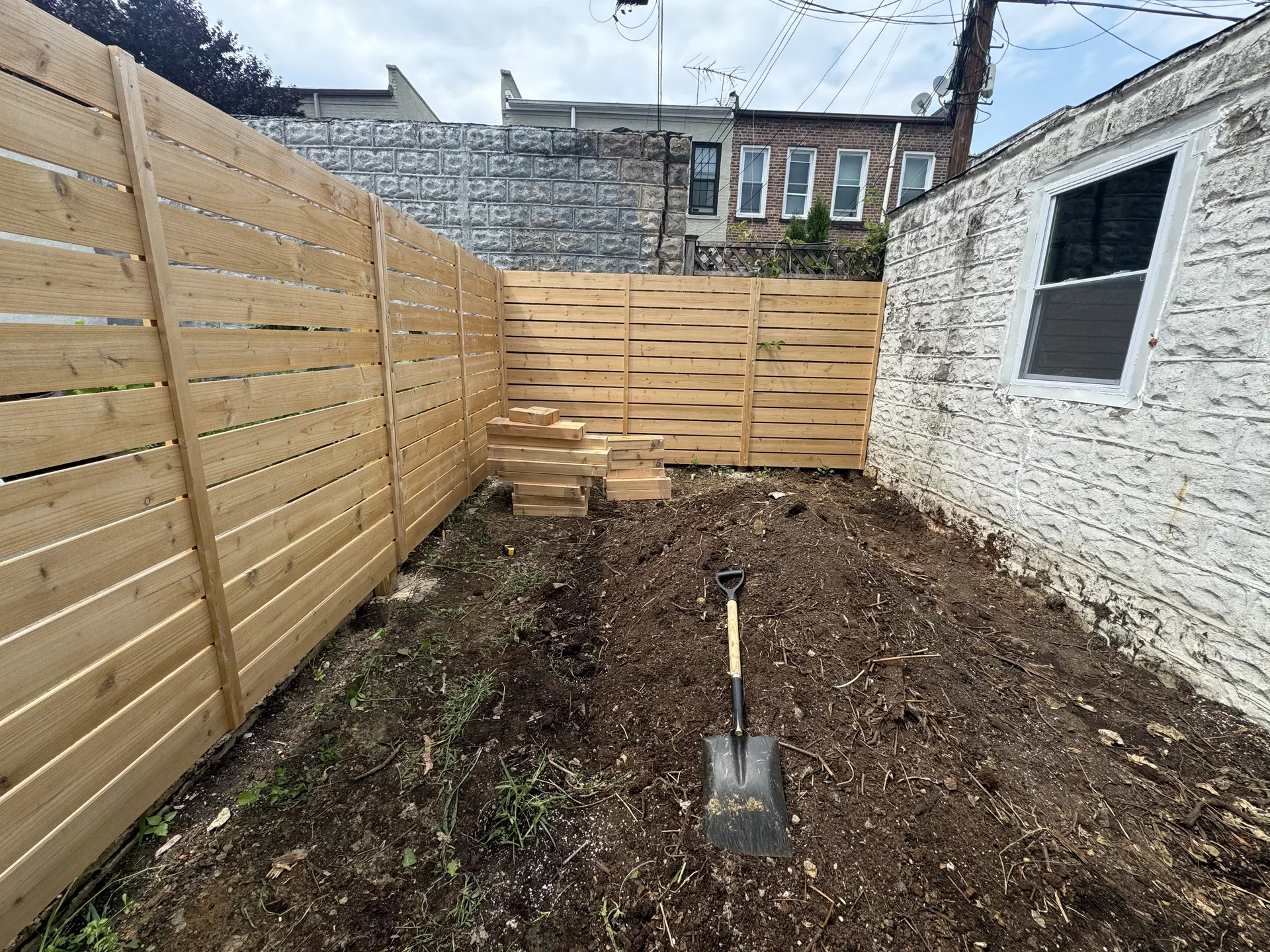 Before photo of bare dirt area and fence with no planter installed
