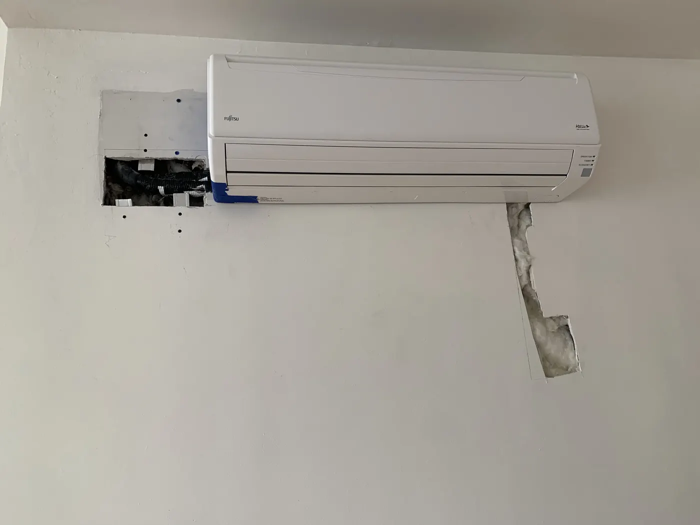 Indoor mini-split unit with drywall damage and open wall cuts before repair