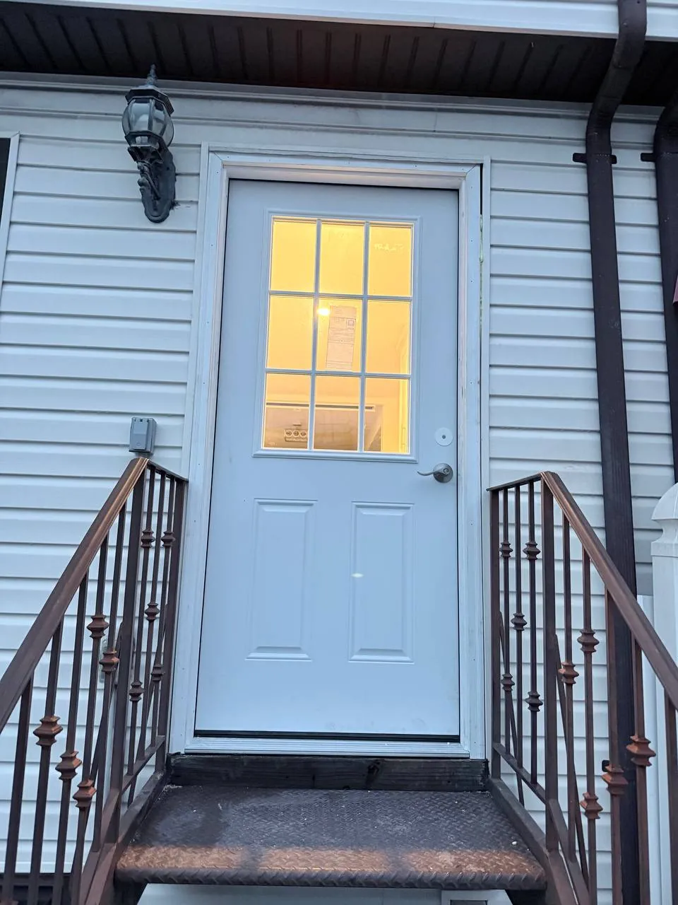 New white entry door installed at a Staten Island home, lit from inside at dusk