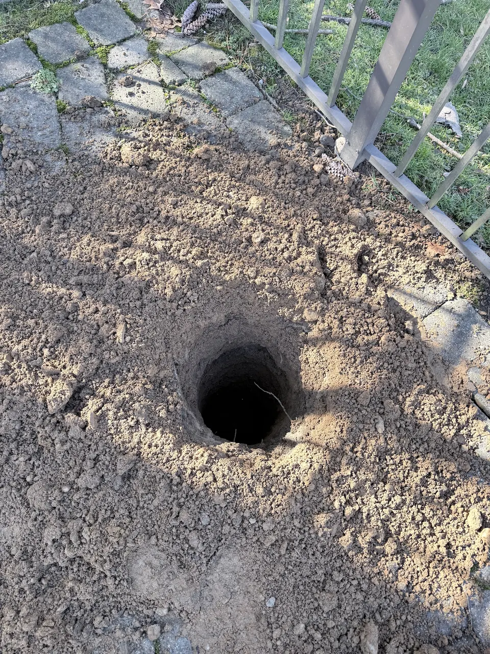 Footing hole drilled and excavated in the ground below a lifted paver