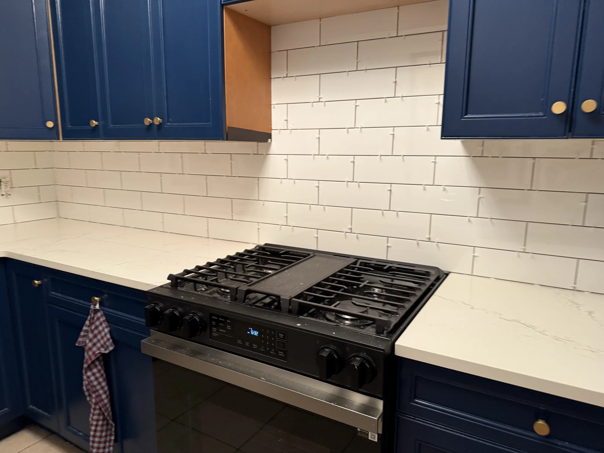 The same wall with the white subway tile backsplash finished, navy cabinets and gas range
