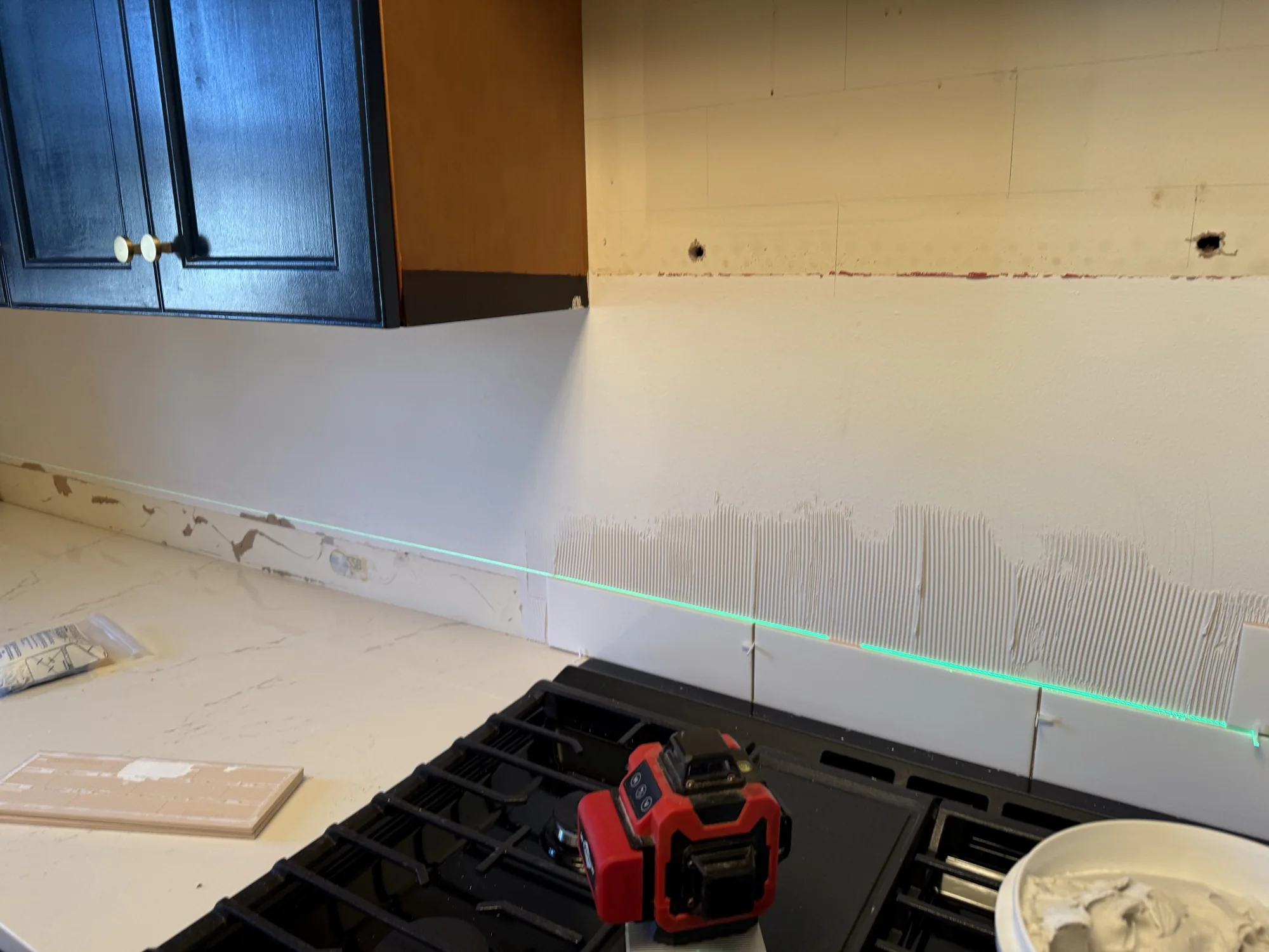 Bare wall between the countertop and navy upper cabinets with a laser line, ready for subway tile, Brooklyn kitchen