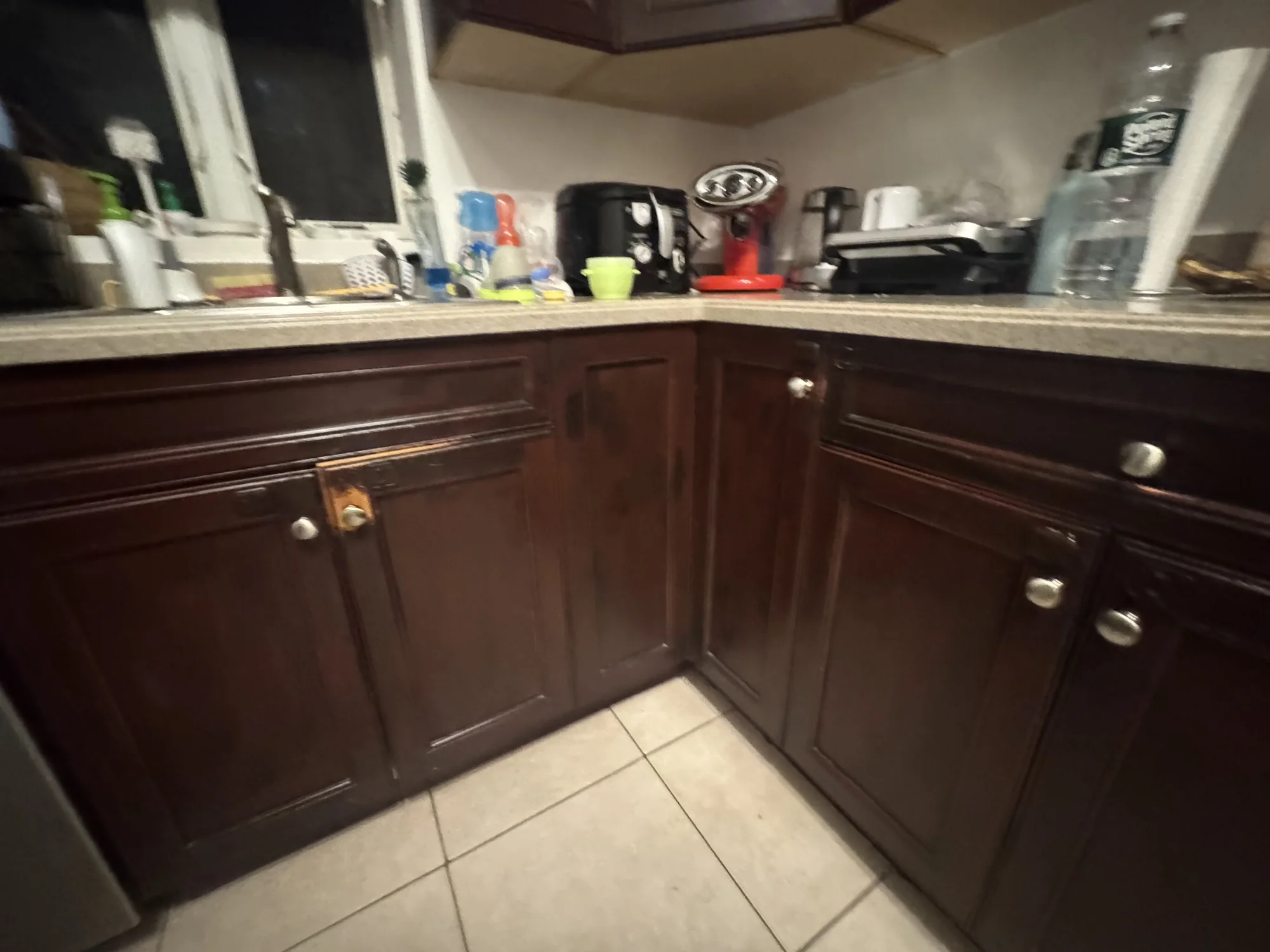 Dark brown base cabinets in the corner of a kitchen with a cream tile floor before the refresh