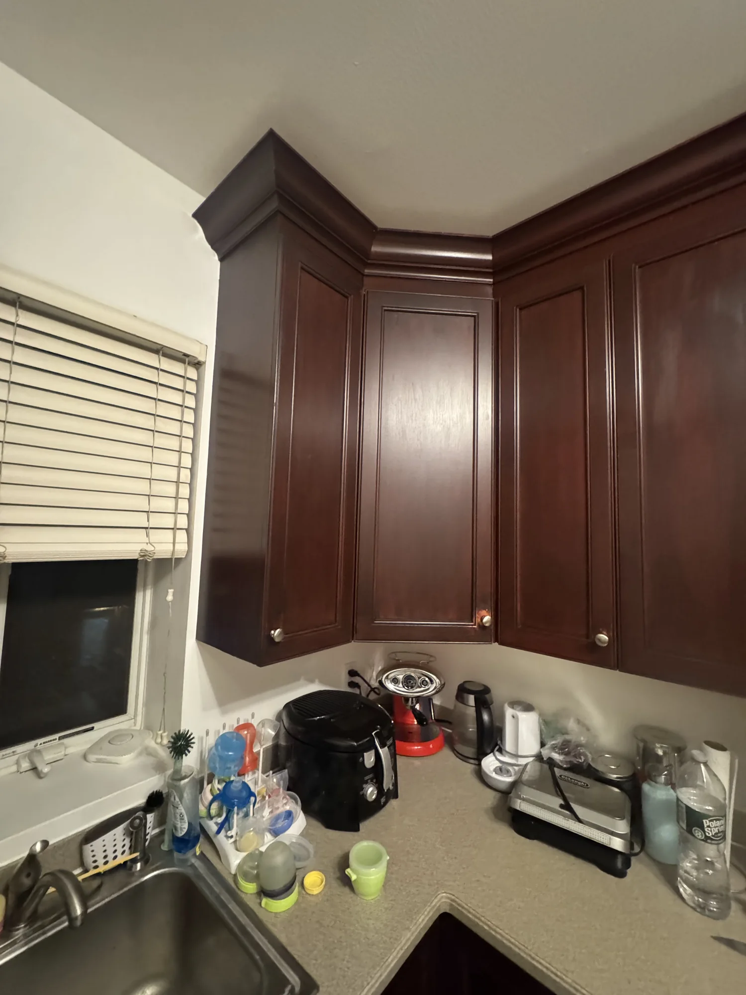 Dark brown corner kitchen cabinets next to a window with white blinds before the refresh, Brooklyn