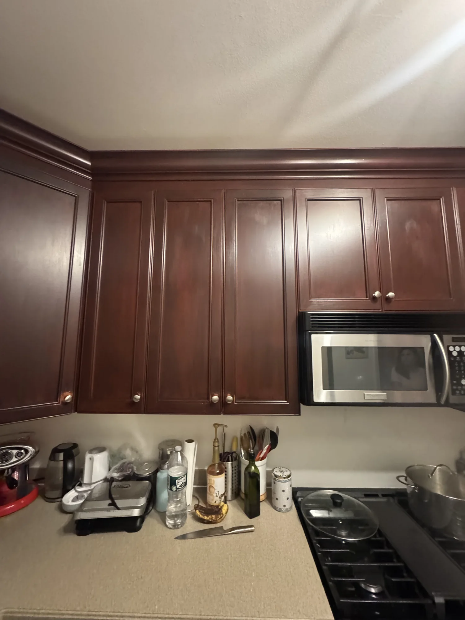 Dark brown kitchen cabinets with a microwave above a gas range before painting, Brooklyn