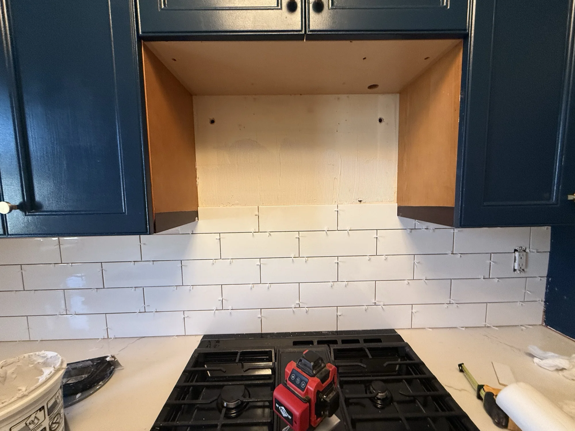 Backsplash half tiled with white subway tile between the countertop and the upper cabinet alcove