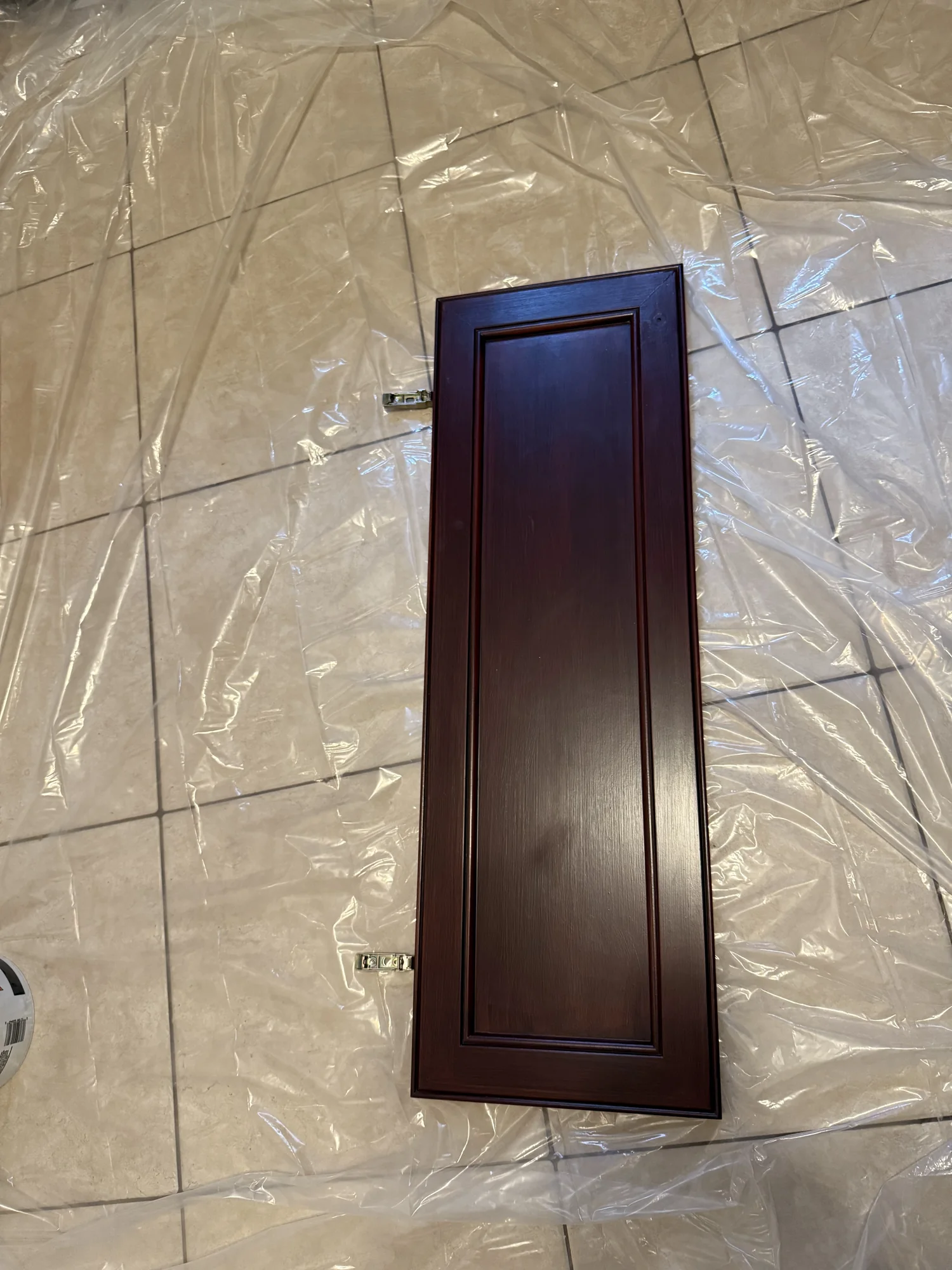 A freshly painted dark cabinet door lying on protective film over a tile floor