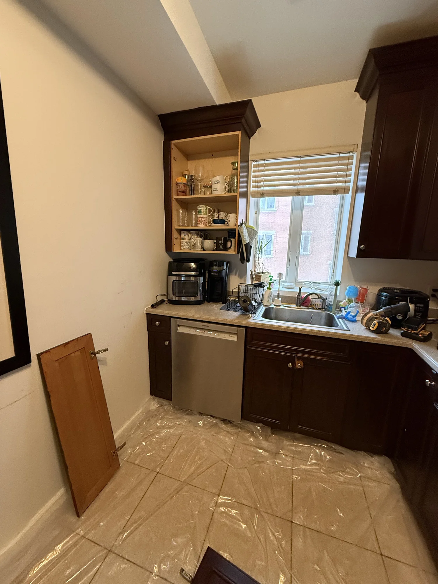 Brown kitchen cabinets with a door removed for stripping, floor covered with protective film, South Slope Brooklyn