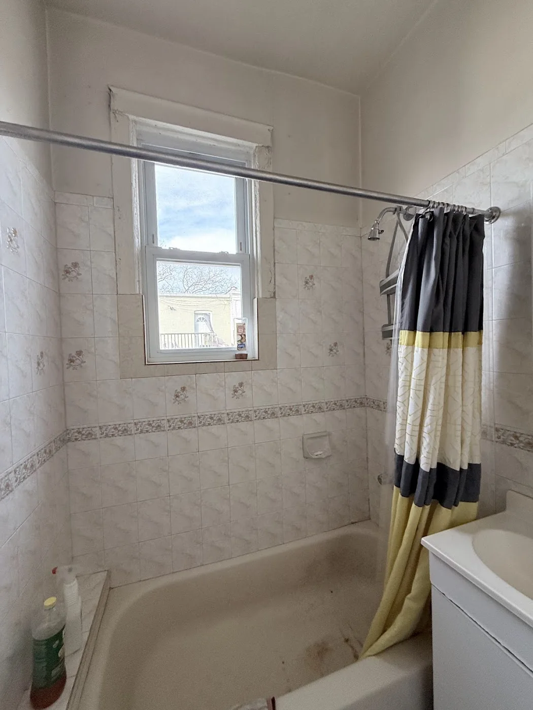 Bathroom before turnover with old shower curtain and dated tub tile condition