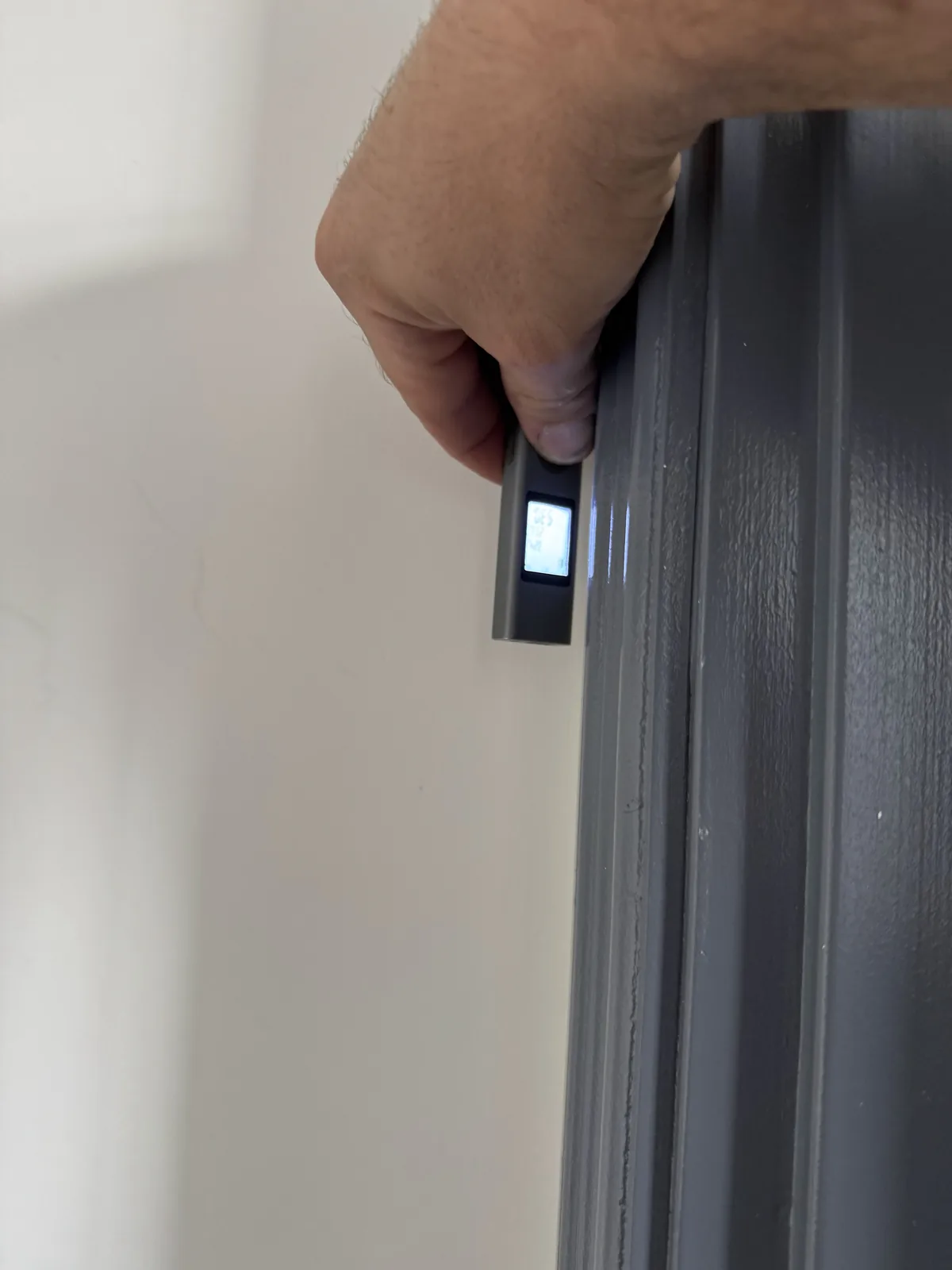 Laser measure checking wall panel alignment near gray trim