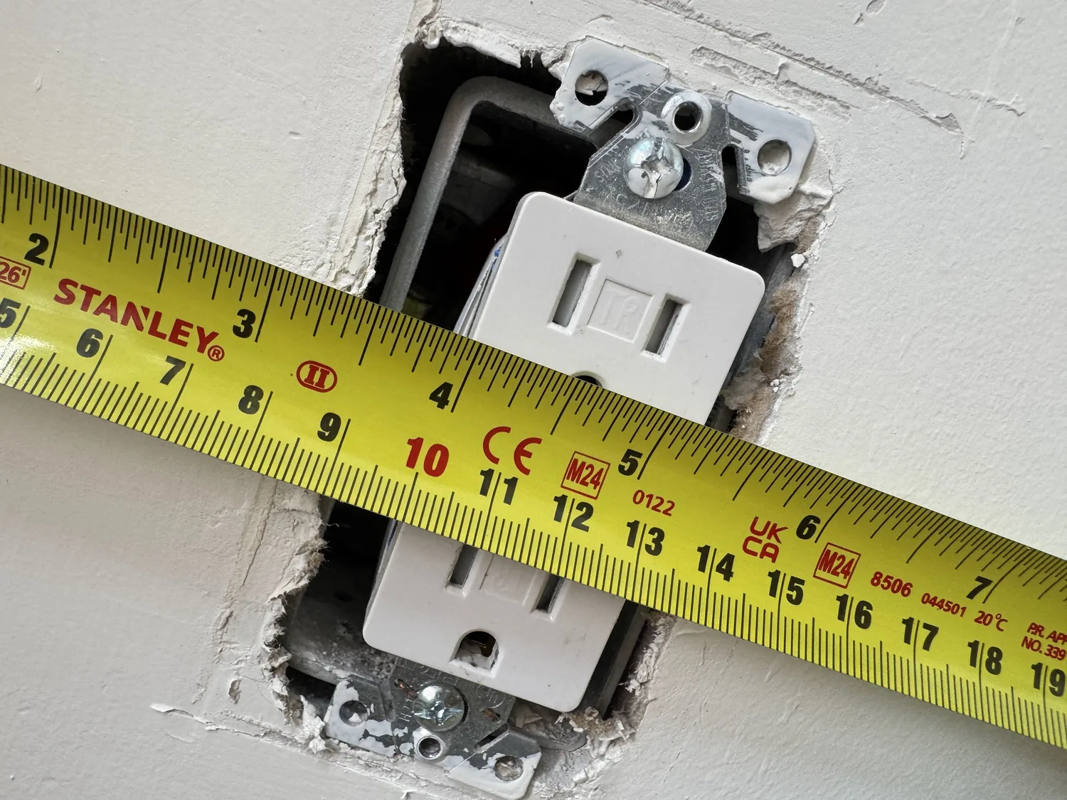 Tape measure checking a receptacle cutout for decorative wall panel installation