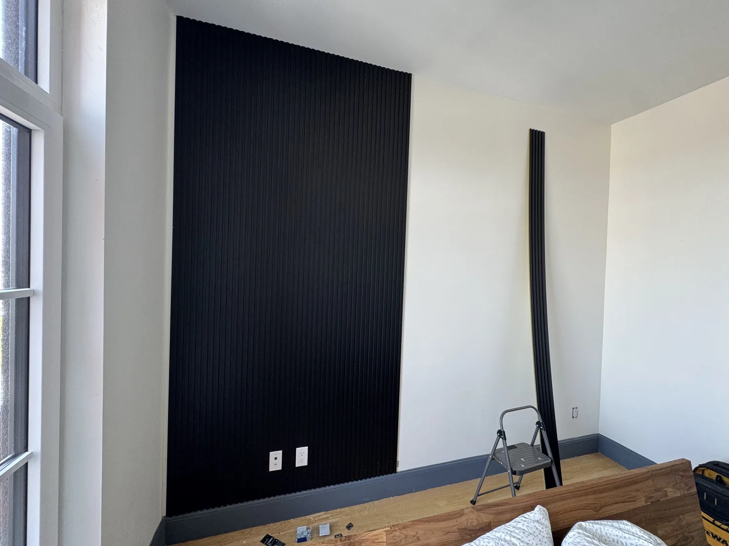 Black plastic wall panels installed on bedroom wall with tools still in the room