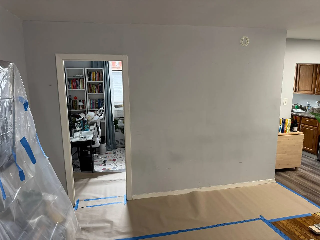 Solid wall with a single narrow doorway to a home office, floor protected with paper, DUMBO Brooklyn apartment