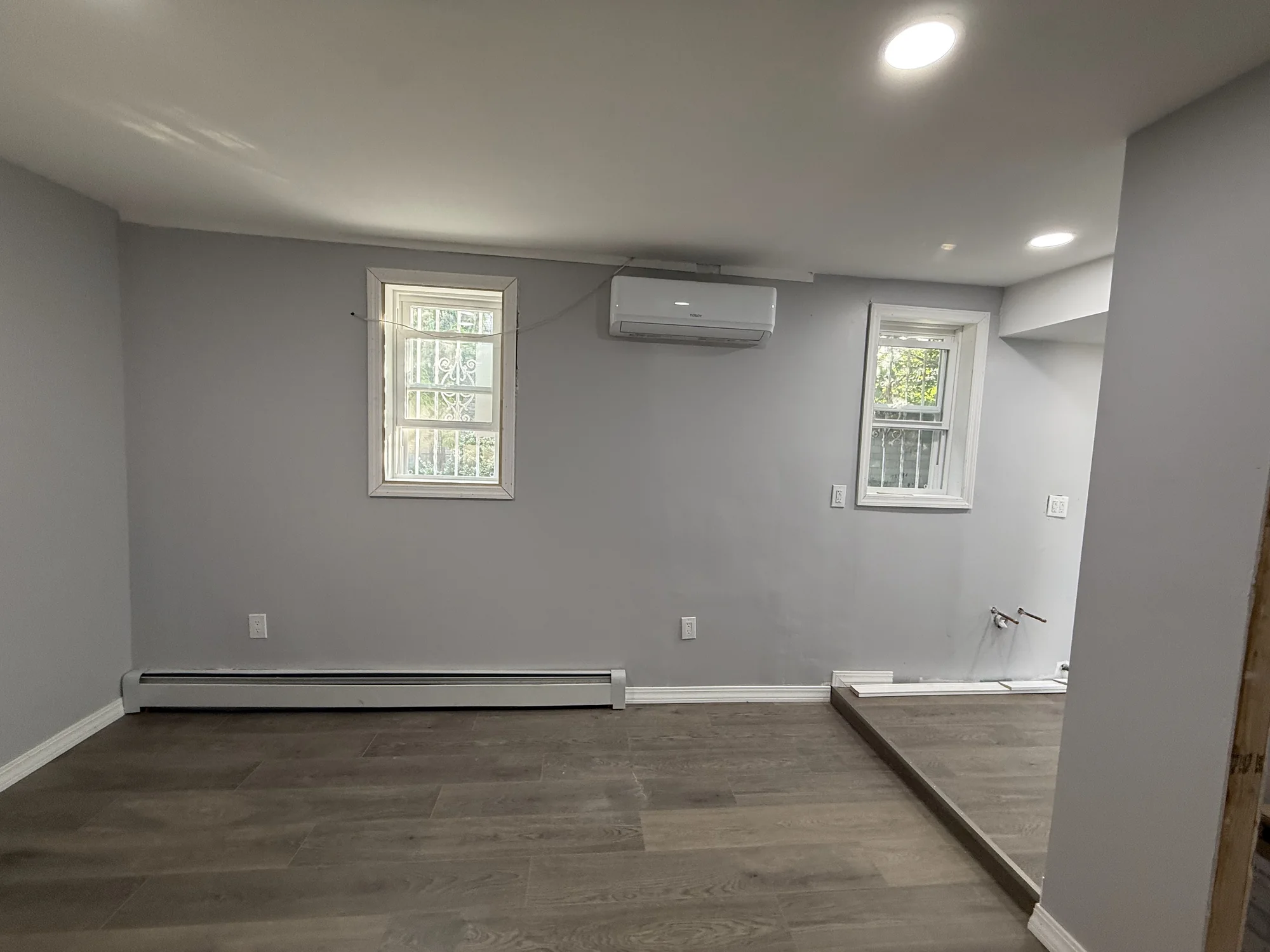 Wide view of the finished room with vinyl plank floor, two windows and a mini-split