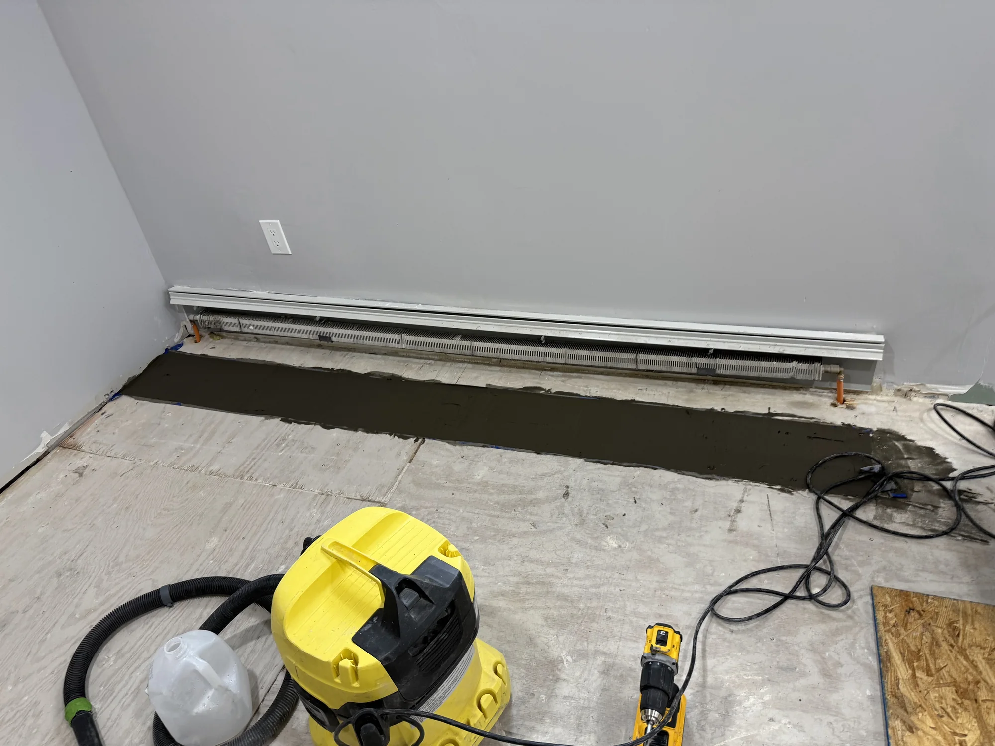 Old uneven floor in a Hollis Queens room before leveling, with tools and a vacuum