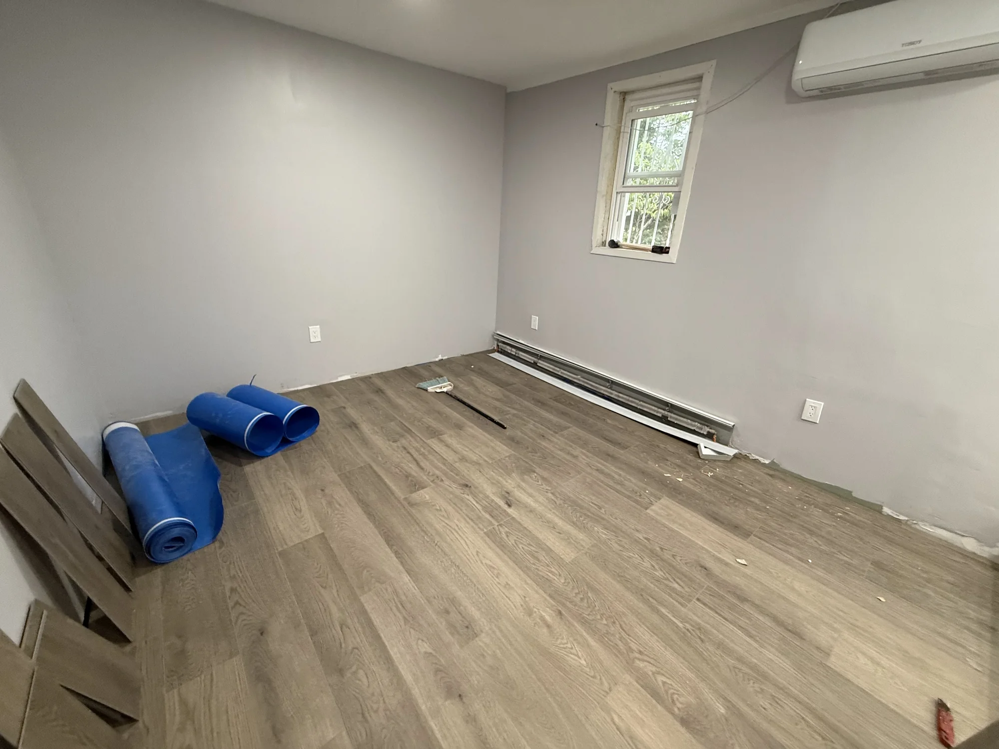 First rows of vinyl plank laid over the underlayment with rolls of underlayment nearby