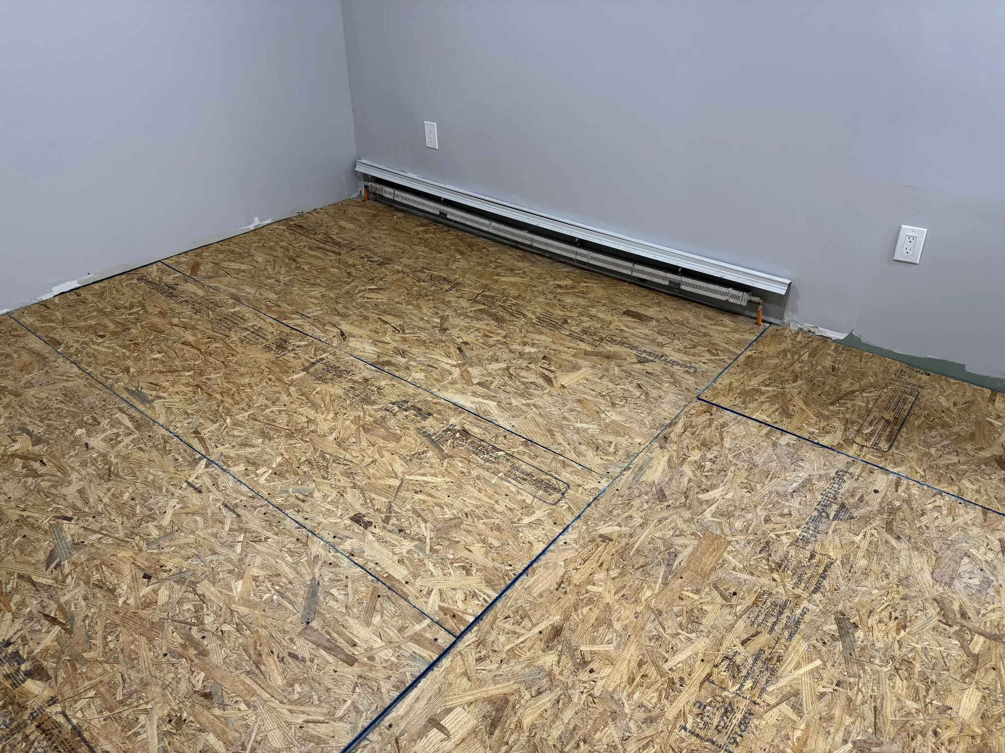 Room fully covered with OSB leveling sheets, baseboard heater on the wall