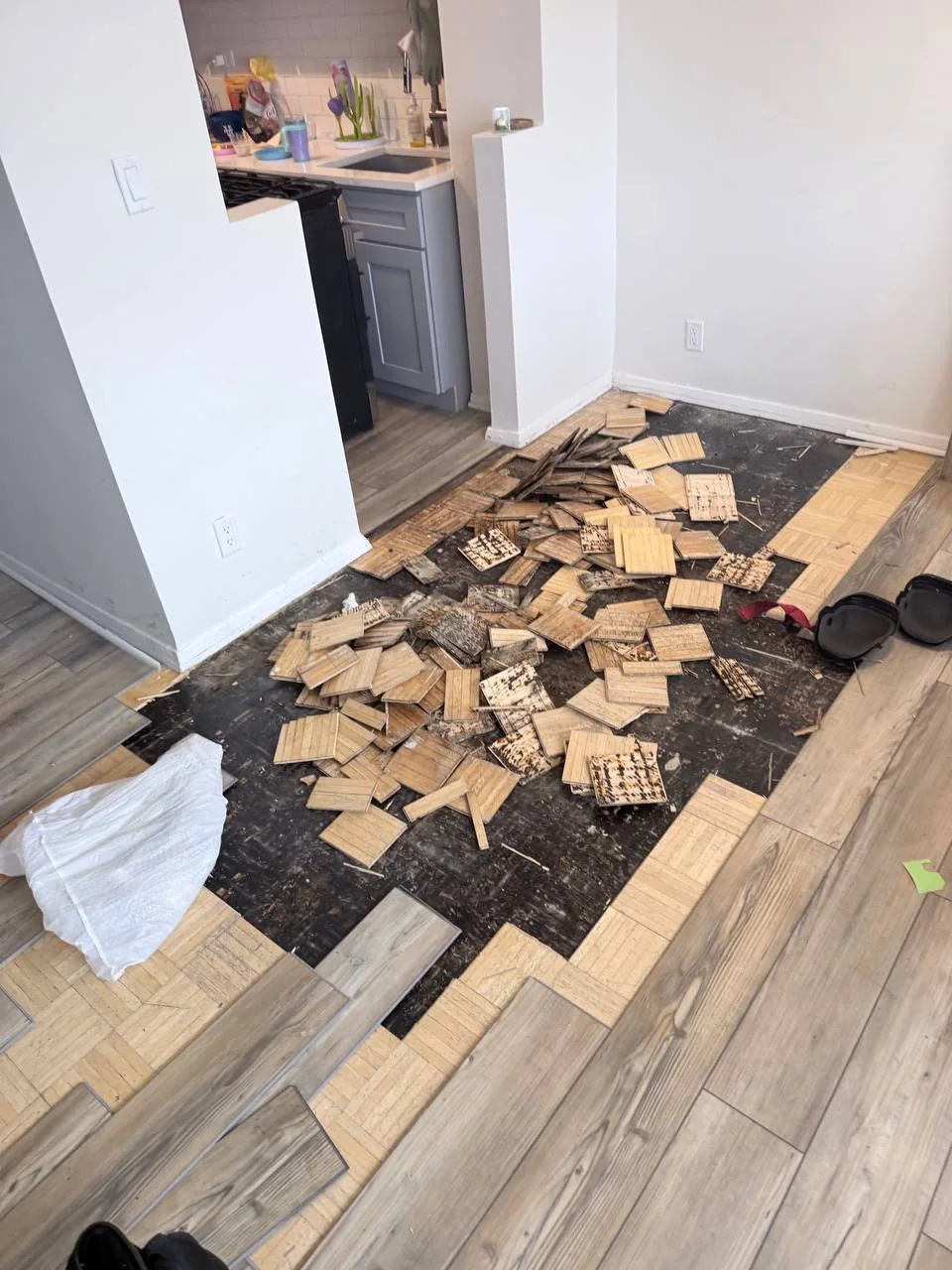 Pile of removed rotted parquet tiles on the bare subfloor of a Bronx apartment after a water leak