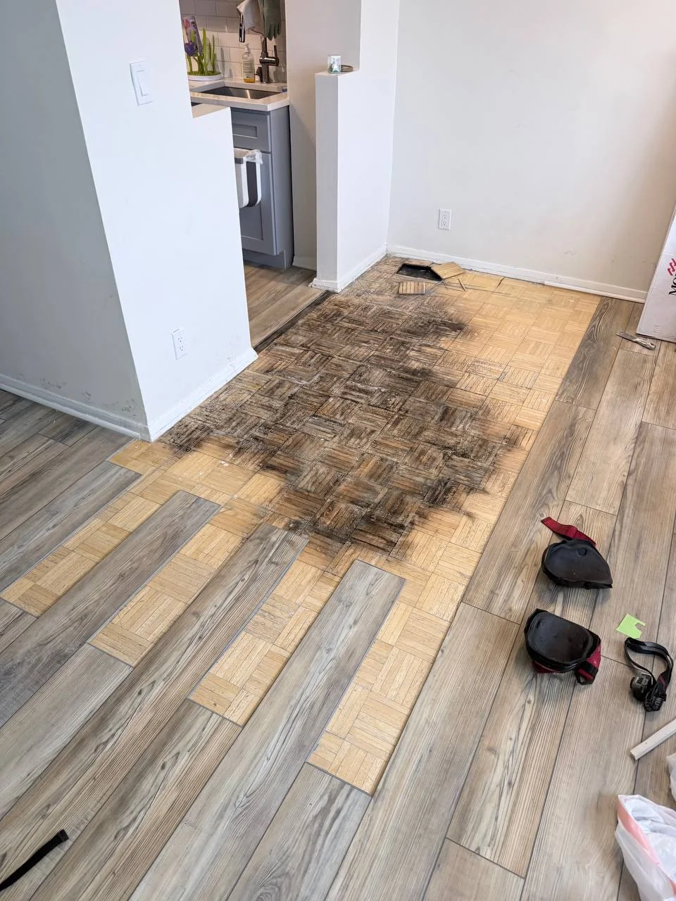 Water-stained, moldy wood parquet subfloor exposed after lifting vinyl planks in a Bronx apartment