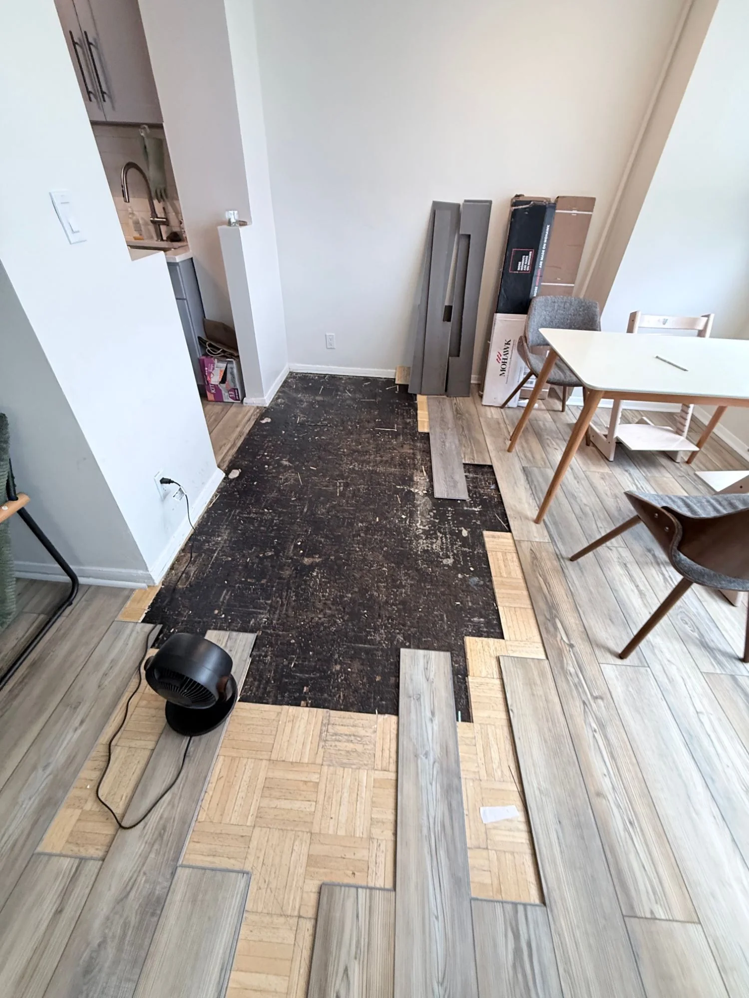 Bare subfloor stripped of parquet with a fan running to dry it out, Bronx apartment living room