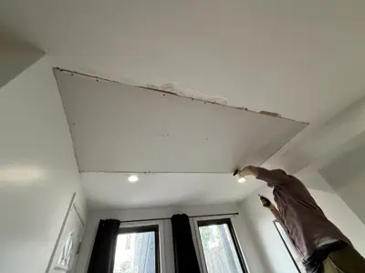 Handyman installing drywall panel on ceiling during repair work in NYC apartment