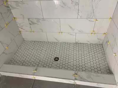 shower tile installation in progress with hex floor tiles and marble wall tiles with leveling clips