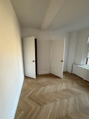 Freshly painted bright room with herringbone hardwood floor pattern and white walls in NYC apartment