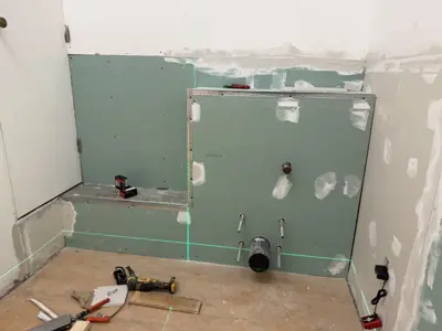 bathroom drywall renovation in progress with green moisture-resistant board and plumbing rough-in visible