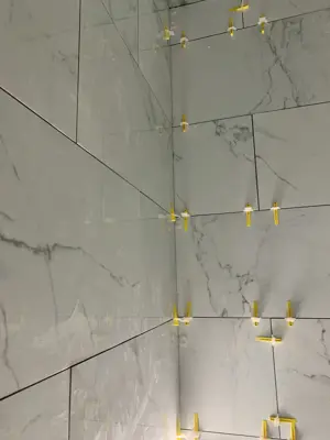 large-format marble-look porcelain tiles being installed with yellow leveling clips on wall