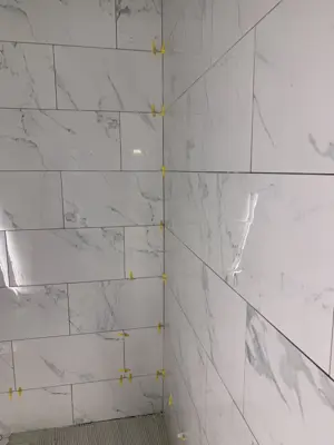 large-format marble-look porcelain tiles being set with leveling spacers in nyc bathroom shower