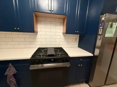completed white subway tile kitchen backsplash with blue cabinets and stainless steel range in nyc