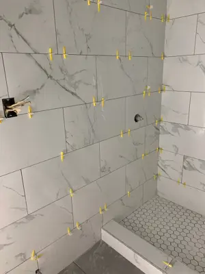 large-format marble-look porcelain tiles being installed in a nyc bathroom shower with yellow leveling clips