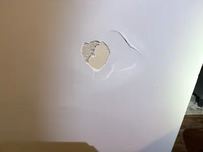 Damaged drywall with fist-sized hole in white wall before repair by Repair ASAP LLC in NYC
