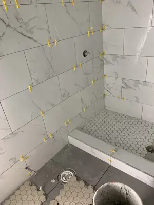 marble-look porcelain tile installation in progress in a nyc bathroom shower with leveling spacers