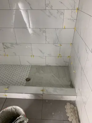 shower floor and wall tile installation in progress with marble tiles and hex mosaic floor tiles in nyc bathroom