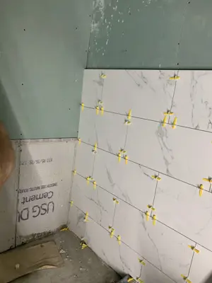 marble-look porcelain wall tiles being set with leveling clips on cement board backer in nyc shower renovation