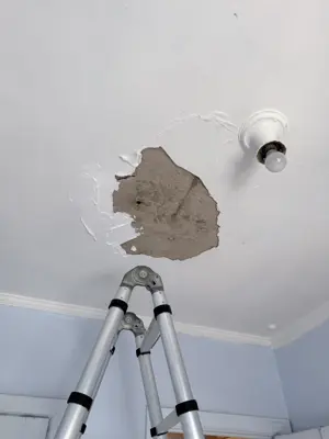 Large hole in ceiling exposing concrete with ladder positioned below for drywall repair in NYC apartment