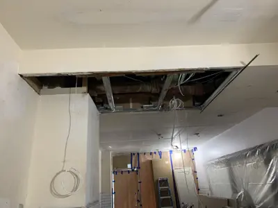 Open ceiling drywall exposing pipes and wiring during renovation repair work in NYC