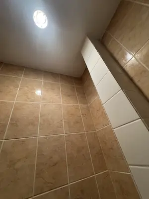 completed bathroom tile installation with beige floor and wall tiles and recessed ceiling light