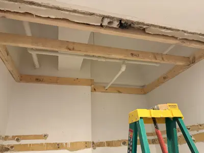 Open ceiling framing with exposed pipes and wood beams during drywall repair process in NYC