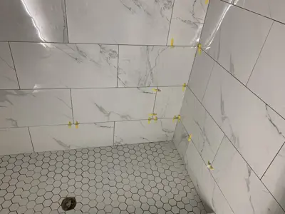 marble-look wall tiles being installed with spacers in a bathroom shower with hex floor tiles